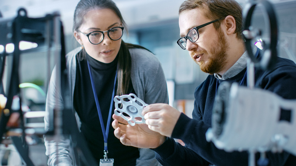 Junge talentierte Ingenieure und Ingenieurinnen diskutieren in einem modernen Labor über einen mit Hilfe eines 3D-Druckers hergestellten Prototyp.